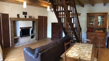 Een rustiek interieur met een houten trap, een open haard, een leren bank en een eettafel.