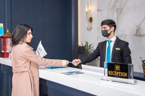 A reception desk with a "RECEPTION" sign, a man in a suit, and a woman handing over a card.
