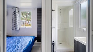A bedroom with a bed, a shower, and a window with a view of trees.