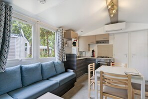 A compact living space with a sofa, dining table, and kitchenette. - Family Mobile Home with Shared Terrace, Private Garden, and Air Conditioning (Les Mathes)