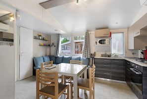 A compact kitchen with a dining table, chairs, and a built-in microwave. - Family Mobile Home with Shared Terrace, Private Garden, and Air Conditioning (Les Mathes)
