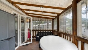A covered porch with a table, a bench, and a sliding glass door leading to a room.