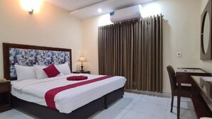 Una habitación de hotel con una cama grande, un escritorio, una silla, una lámpara y una cortina.