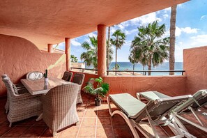 An outdoor patio with wicker furniture, a table, and lounge chairs, overlooking palm trees and the sea. - Bb.b5 - Spacious Apartment With Amazing View (Estepona)
