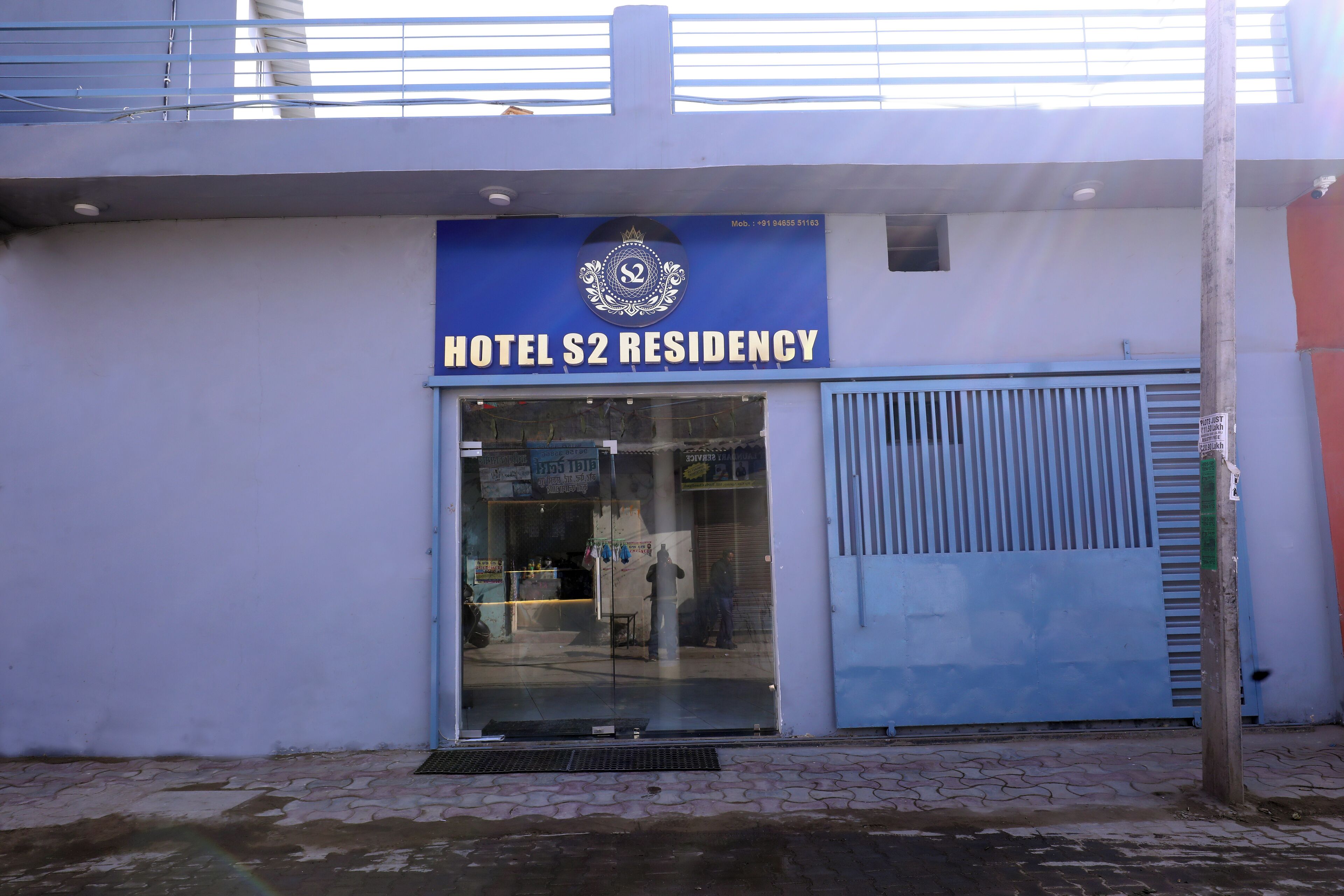 The exterior of Hotel S2 Residency with a blue sign, a glass entrance, and a metal gate.