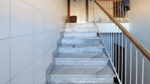 Una escalera con escalones de mármol blanco y barandilla de madera, que conduce a una plataforma con una puerta y un ventanal pequeño.