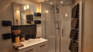 Une salle de bain moderne avec une douche à l’italienne en verre, un lavabo blanc doté d’un plan de toilette noir et un grand miroir.