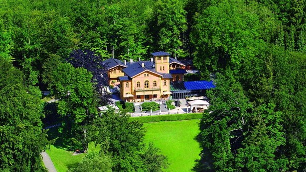 Un chalet au bord du lac, avec un grand bâtiment entouré d’une végétation luxuriante, une jetée qui s’avance dans l’eau et une pelouse bien entretenue.