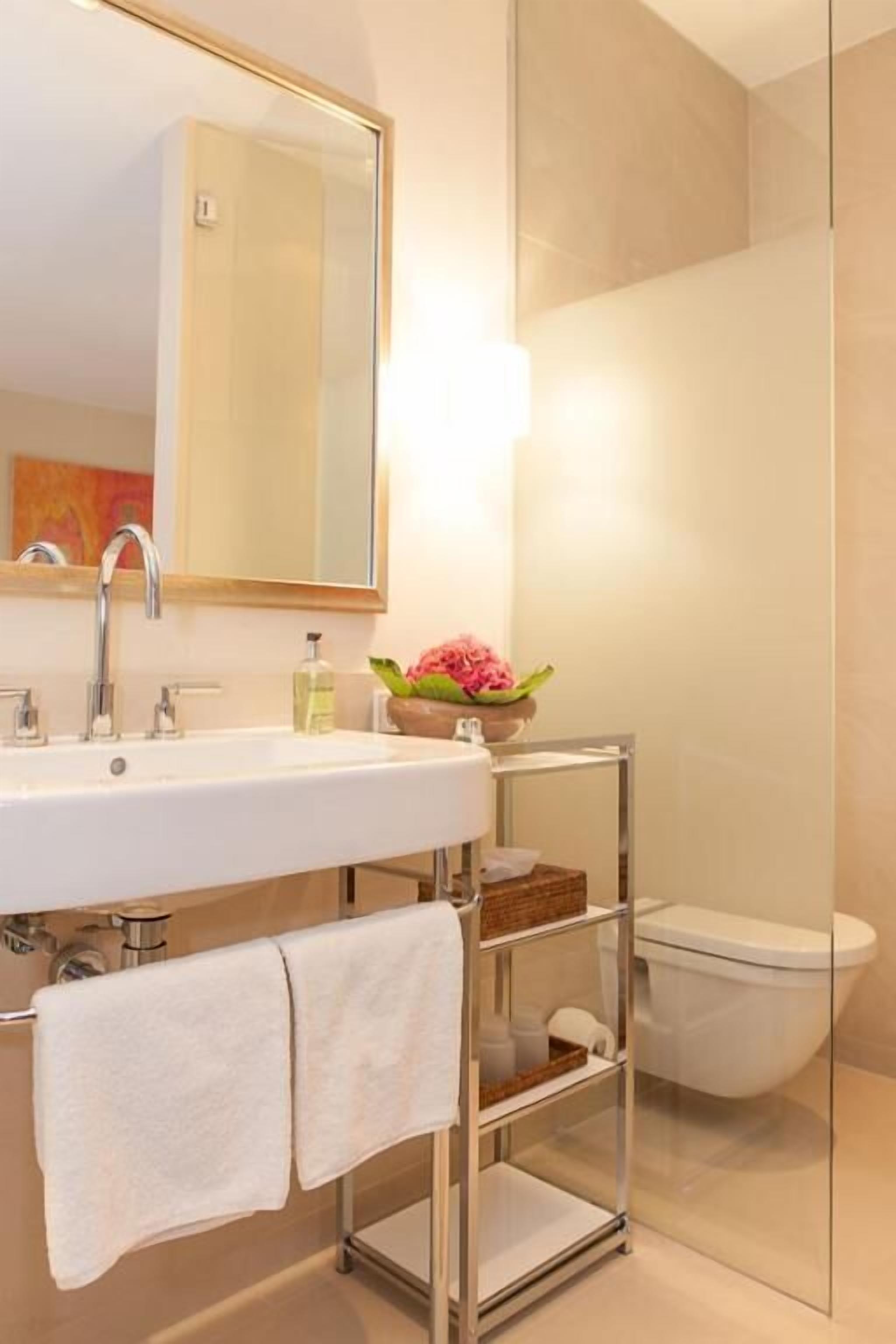 Ein modernes Badezimmer mit einem weißen Waschbecken, einem Spiegel, einer Duschkabine aus Glas und einer Toilette.