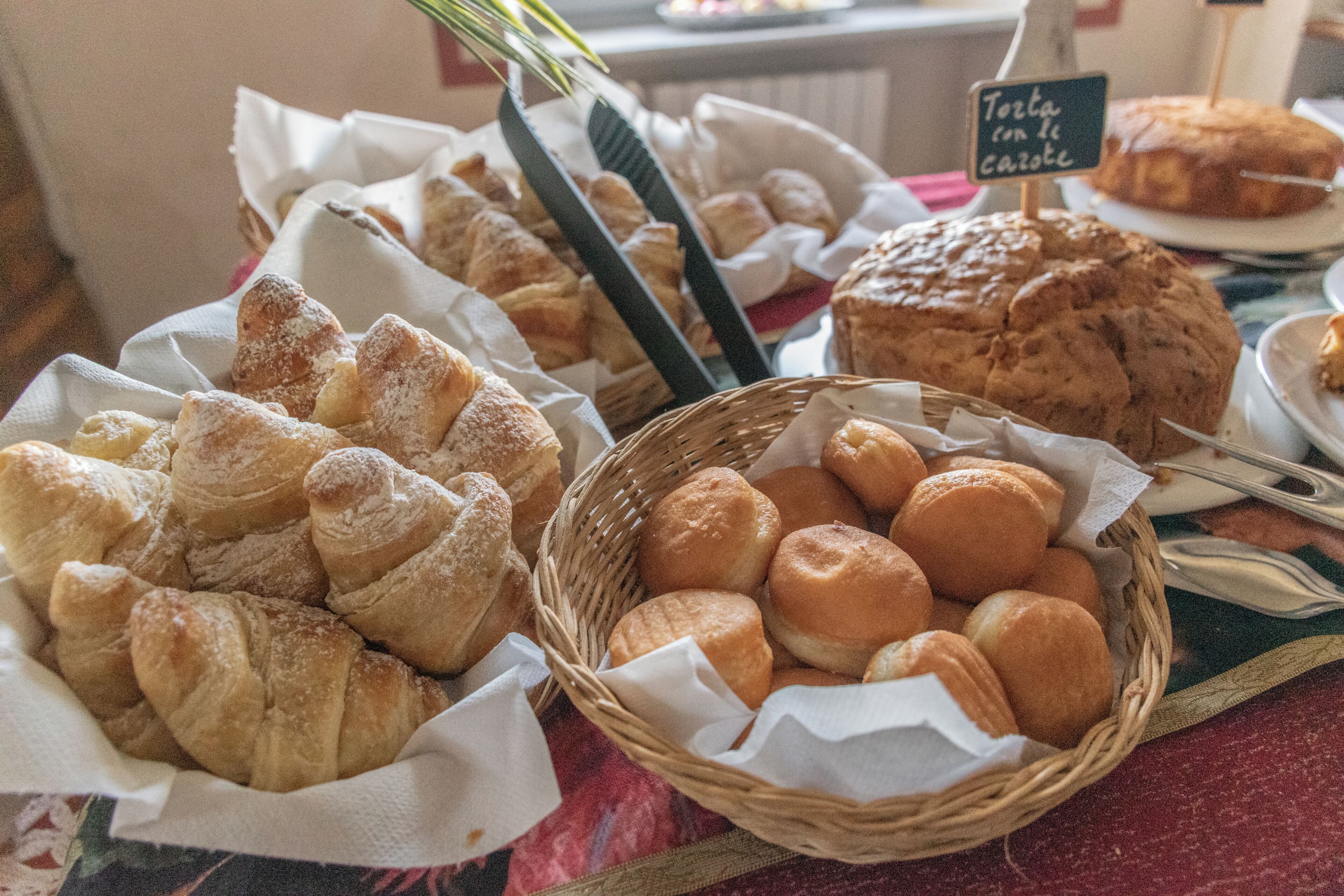 Une variété de produits de boulangerie présentés dans des paniers et sur des assiettes, ce qui évoque l’ambiance d’une boulangerie ou d’un café.