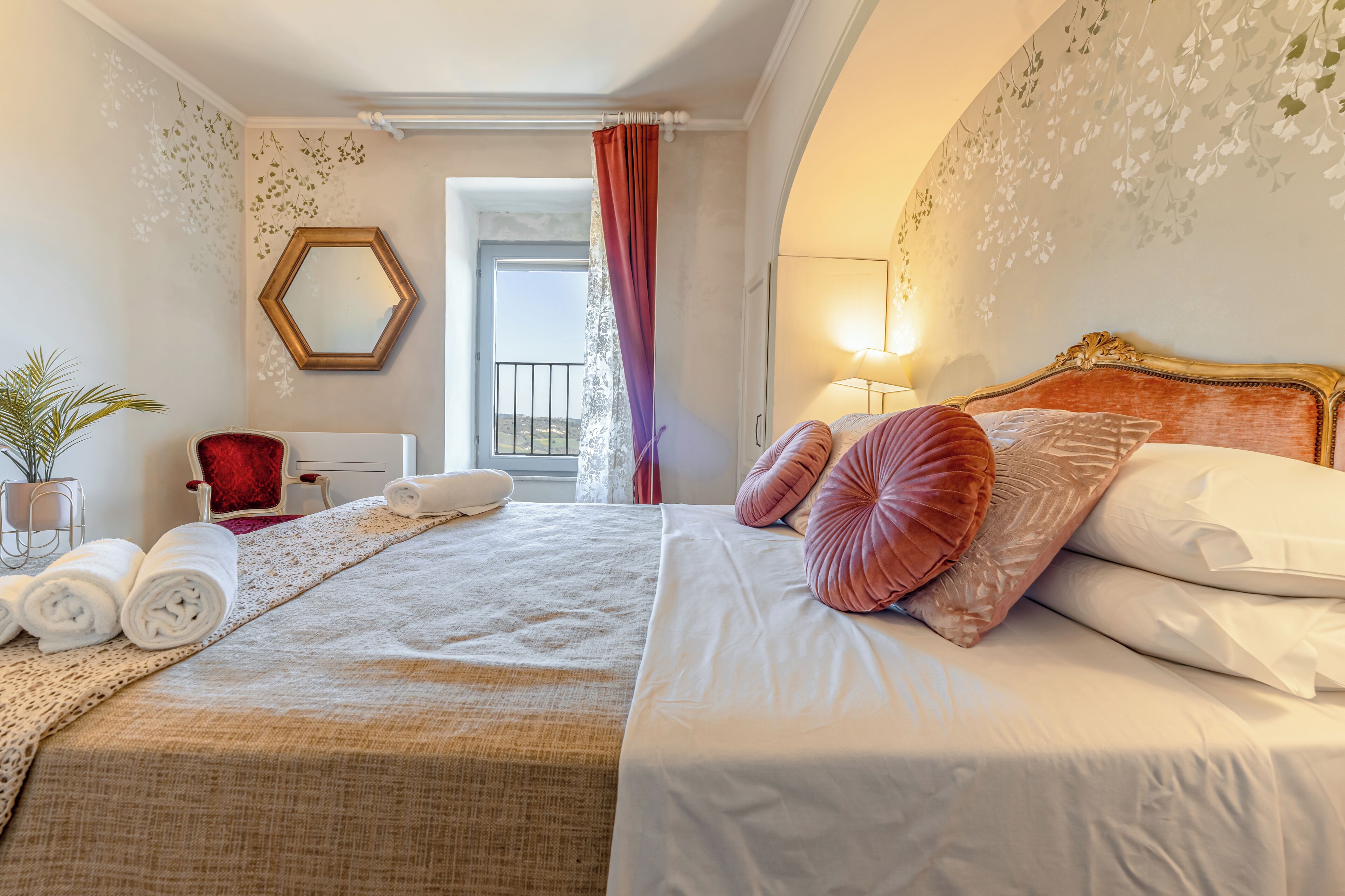 Une chambre d’hôtel avec un lit, une chaise, un miroir, une plante en pot et une vue sur l’extérieur.