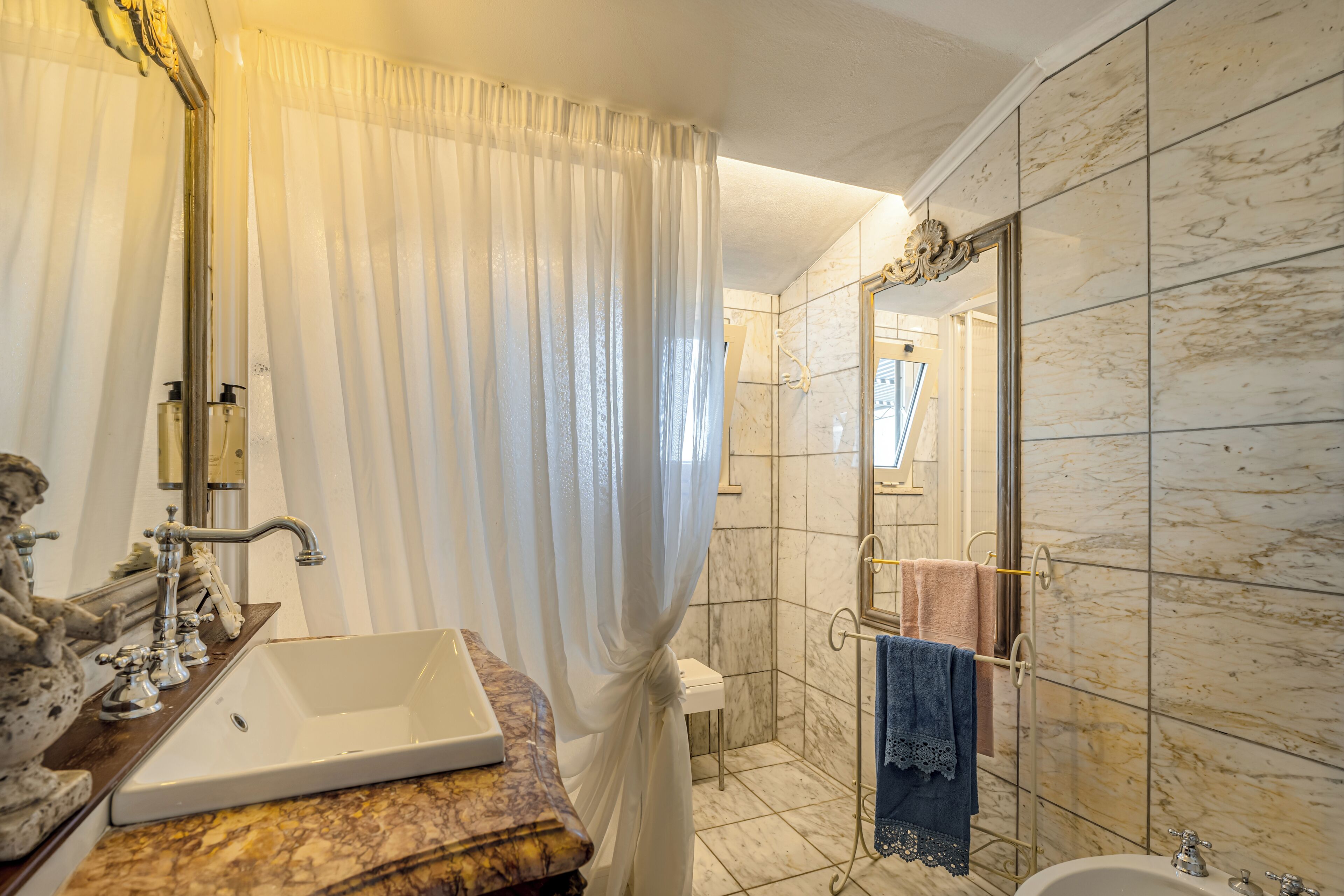 Ein Badezimmer mit einer Marmordusche, einem Waschbecken mit Spiegel und einem Handtuchhalter.