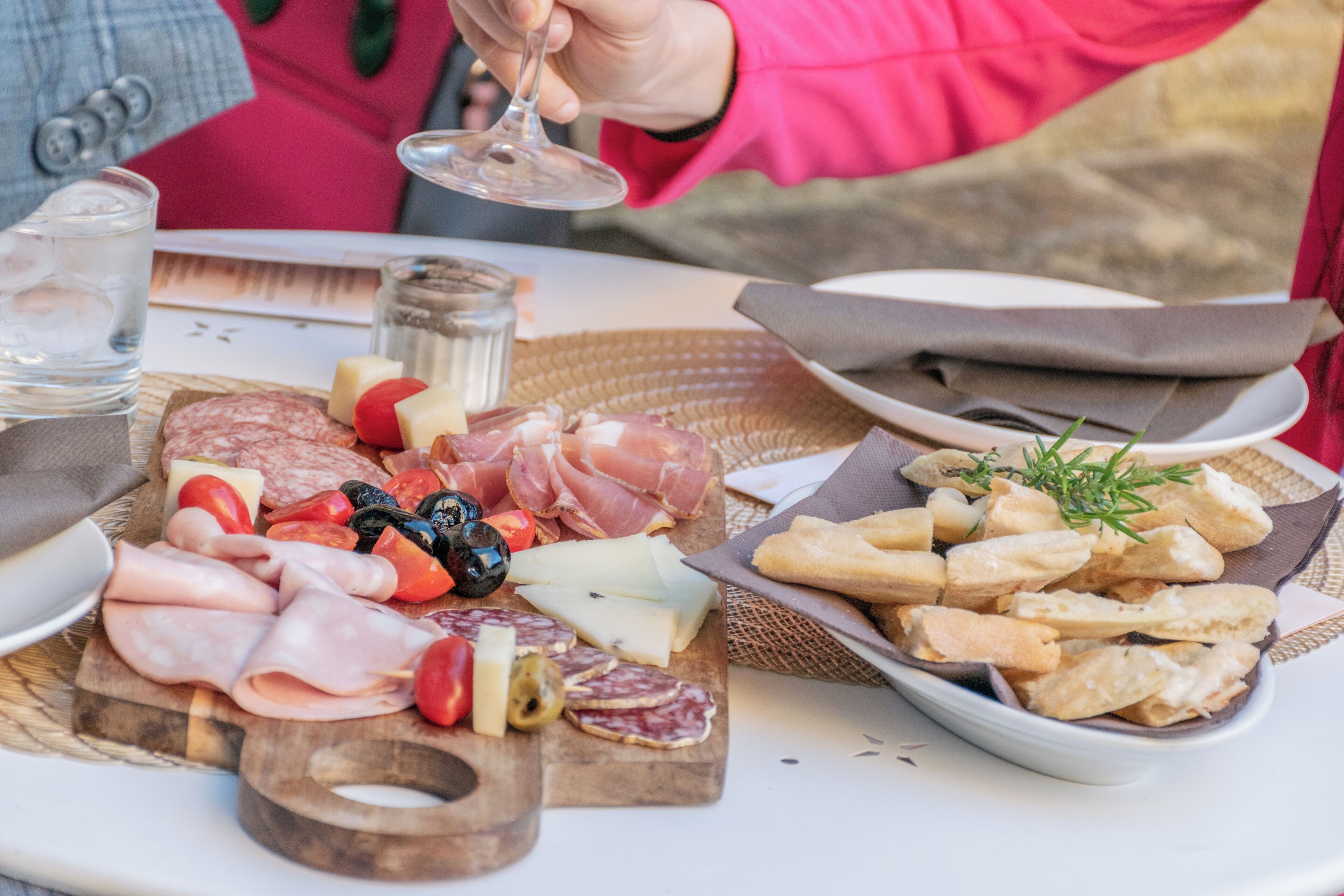 A table with a variety of cheeses, cured meats, and bread, accompanied by a glass of water and a wine glass.