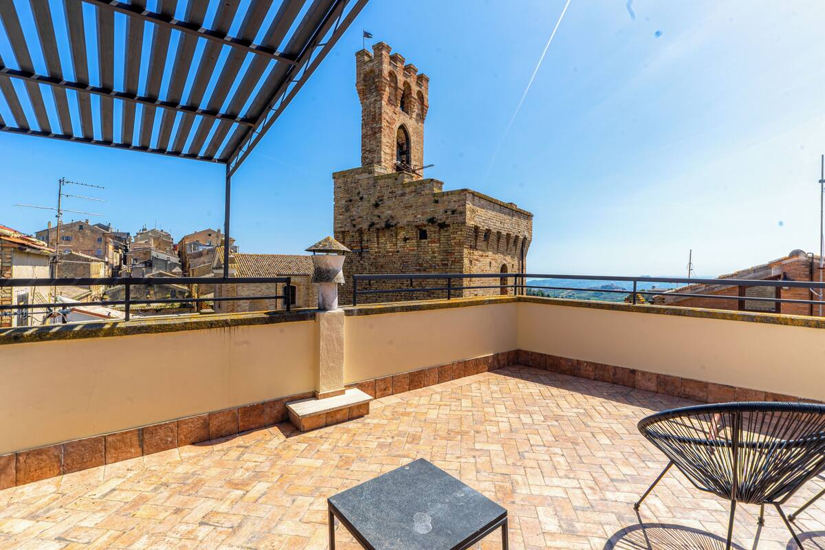 Eine Dachterrasse mit Blick auf einen historischen Turm, einem kleinen Tisch und einem Stuhl.