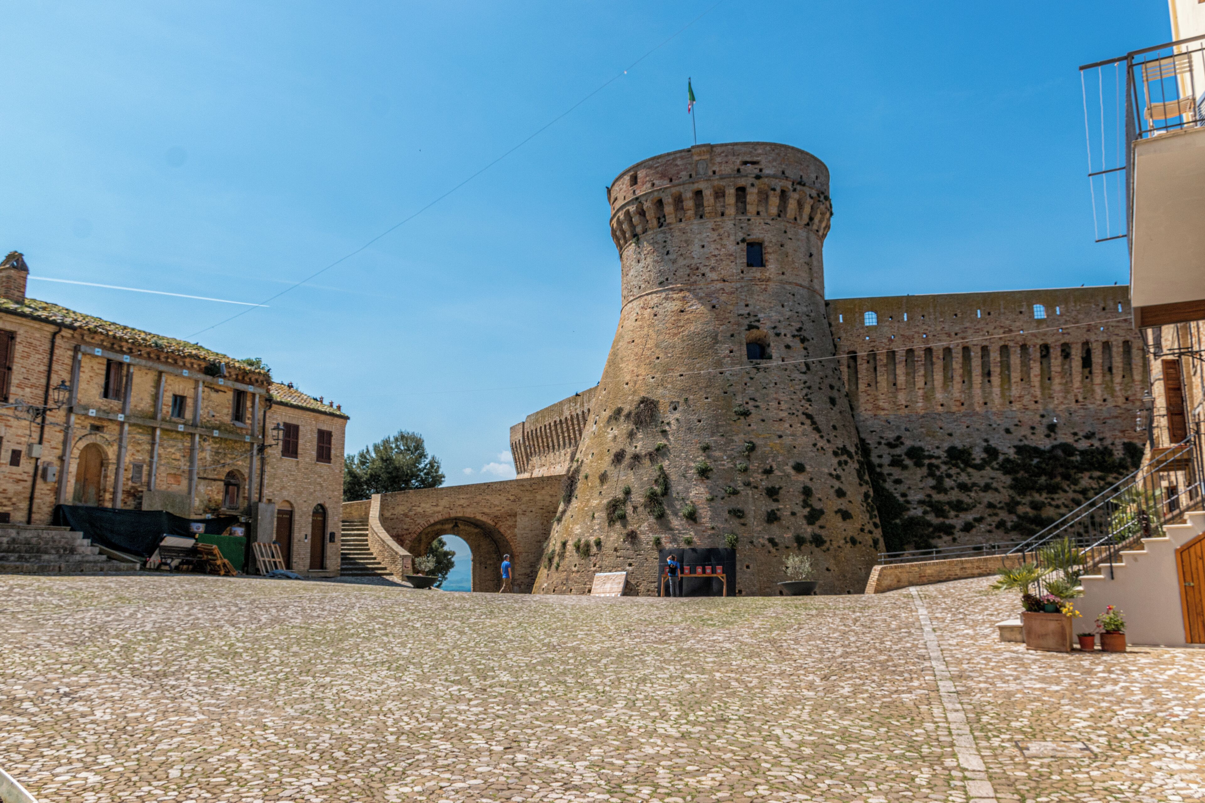 A historic stone tower with a flag, a cobblestone courtyard, and a building with an archway.