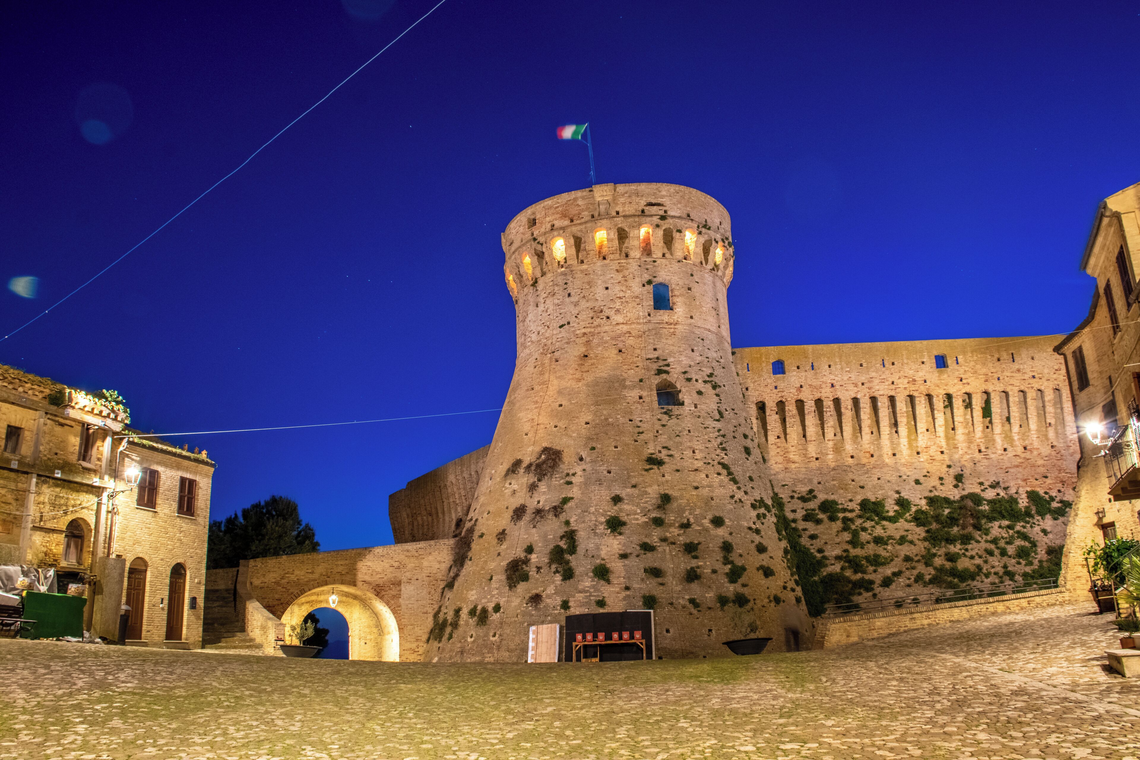 Ein historischer SteinTurm mit einer Flagge, ein Kopfsteinpflasterhof und ein Gebäude mit Bogenportal.