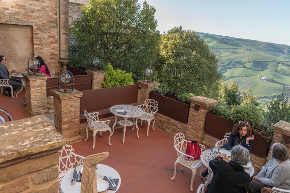 An outdoor patio with tables and chairs, a brick wall, and a view of the countryside. - Hotel Oviv Dimora del borgo (Acquaviva Picena)