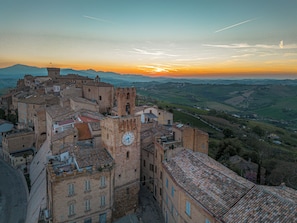 Eine historische Stadt mit mittelalterlicher Architektur, darunter ein markanter Glockenturm, umgeben von sanften Hügeln und einem Sonnenuntergang.