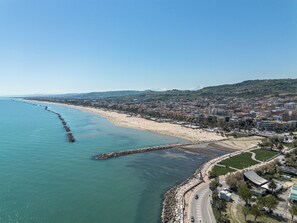 Une vue aérienne d’une ville côtière, avec une plage, une longue jetée et un mélange de bâtiments résidentiels et commerciaux.