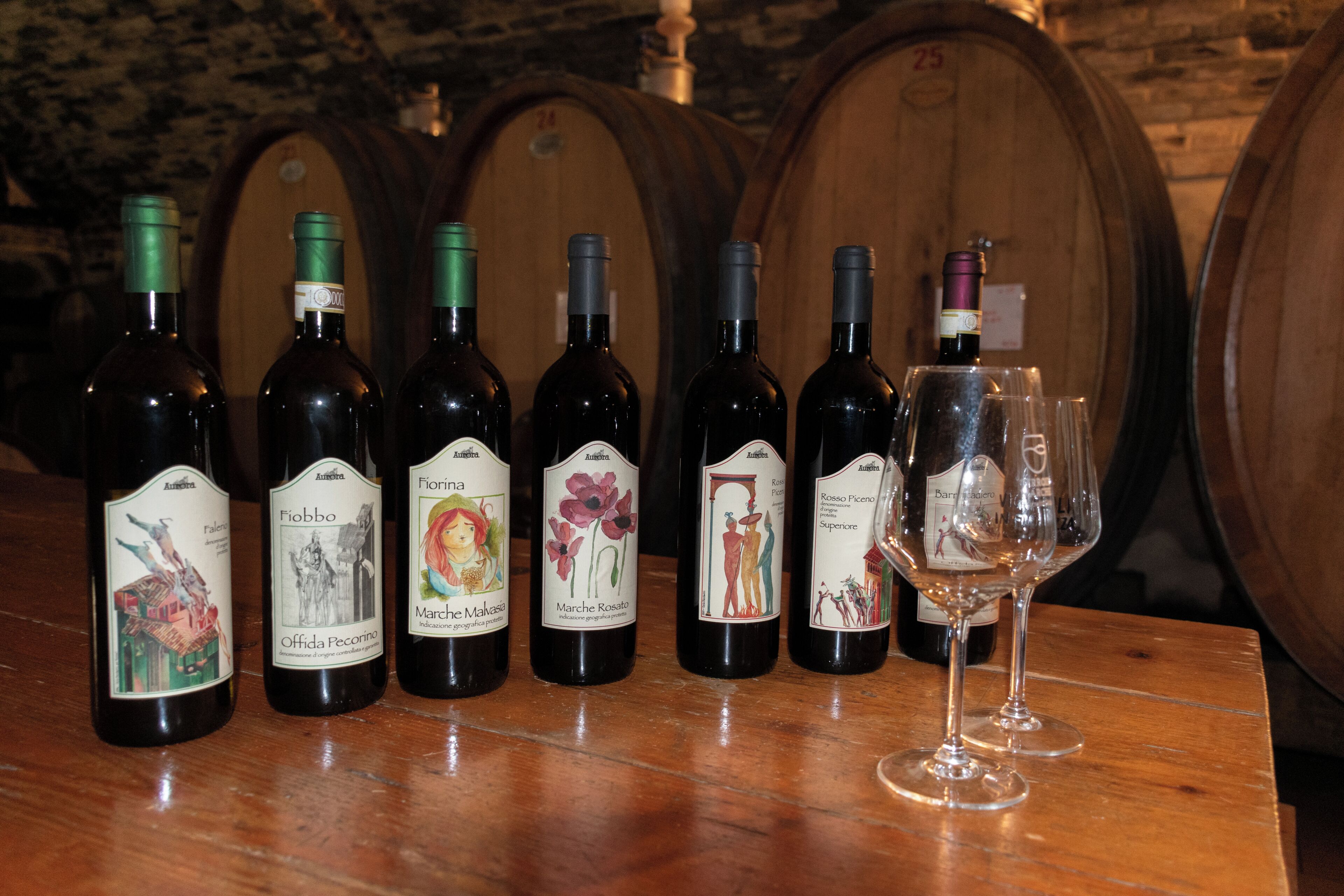 Des bouteilles de vin et un verre à vin sont posés sur une table en bois, avec des barriques en arrière-plan.