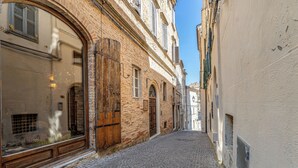 A narrow cobblestone street flanked by historic buildings with large windows and wooden shutters. - Hotel Oviv Dimora del borgo (Acquaviva Picena)