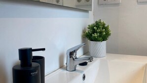 Ein modernes Badezimmer mit einem weißen Waschbecken, einem Chrom-Wasserhahn, einem schwarzen Seifenspender und einem kleinen Topfpflanzen.