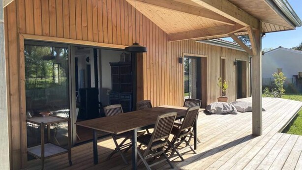 A wooden deck with a table and chairs, a pergola, and a sliding glass door leading to a covered area. - House in Hourtin With Enclosed Garden (Hourtin)