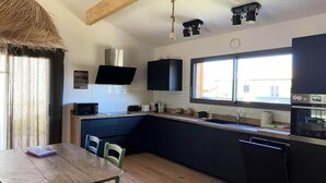 A modern kitchen with dark cabinetry, a wooden dining table, and a large window providing natural light. - House in Hourtin With Enclosed Garden (Hourtin)