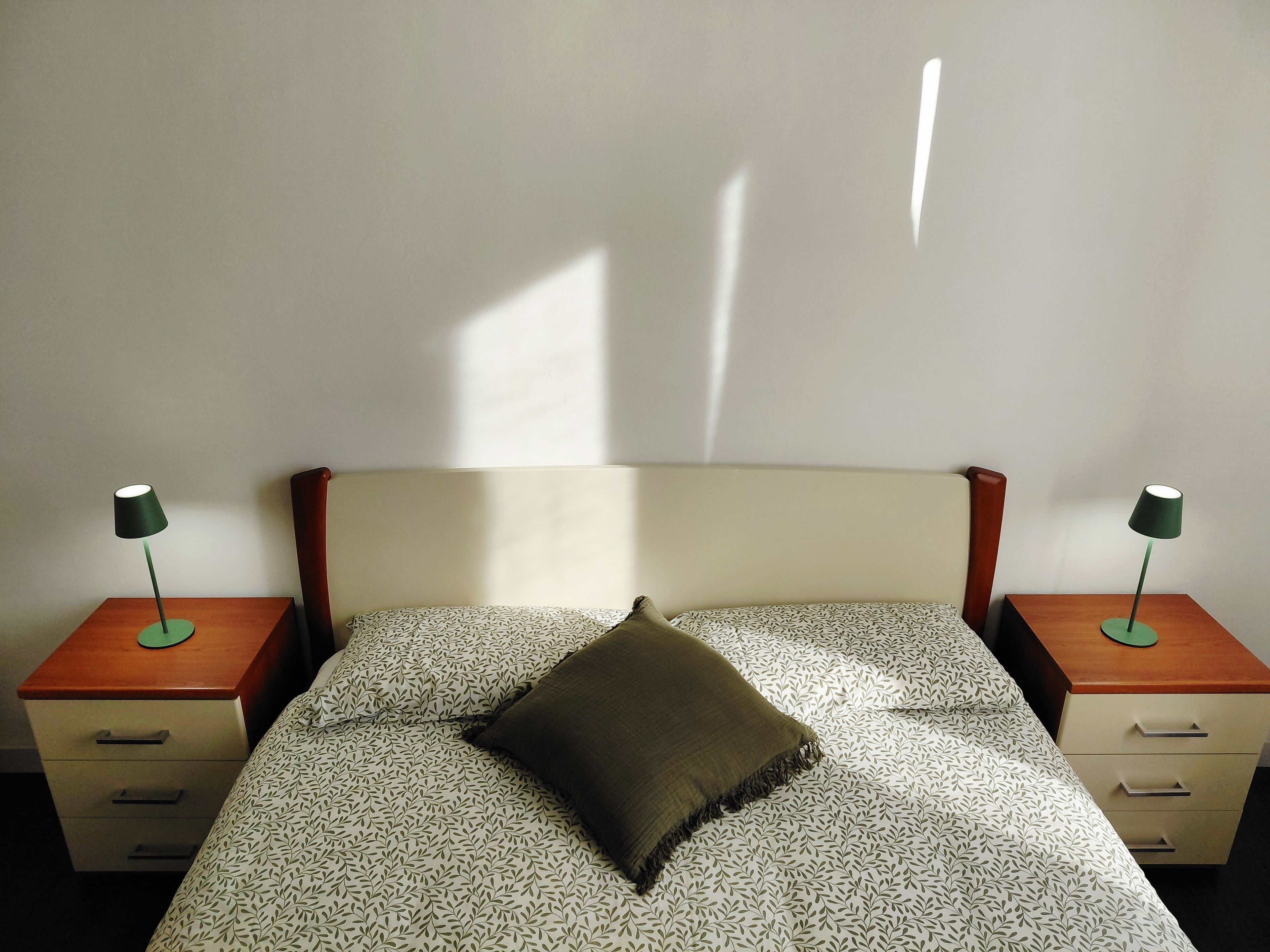 A bed with a patterned bedspread, a single pillow, and two bedside tables with lamps.
