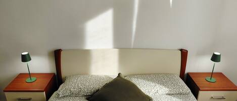 A bed with a patterned bedspread, a single pillow, and two bedside tables with lamps.