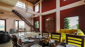 Un vaste espace dédié à la salle à manger, avec un plafond haut, un escalier et un canapé jaune.