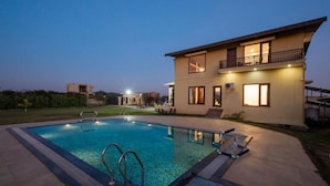 Une maison moderne à deux étages, dotée d’une piscine, de mobilier d’extérieur et d’un balcon bien éclairé.