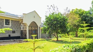 A building with a stone facade, a gated entrance, and a well-maintained garden with various trees and shrubs. - Everlasting Gardens Kitui (Kitui)