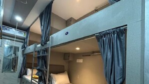 A bunk bed room with curtains, a small window, and a light switch on the wall. - Merhaba Hostel And PG (Mumbai)