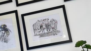 A wall with multiple framed artworks, including a drawing of cows and a plant in a pot.