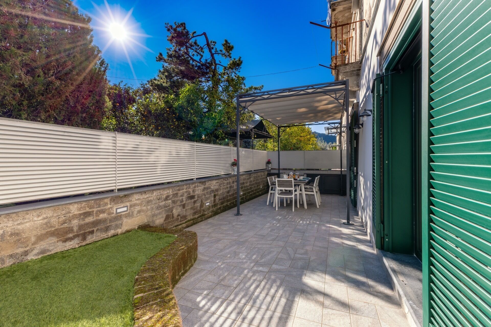Un patio con zona de estar cubierta, pared de ladrillo y puerta verde.