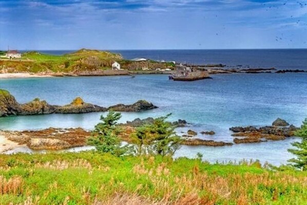 A coastal landscape with rocky outcrops, a white building, and a body of water. - Bree House Sleeps 16 With Free Parking (Malin)
