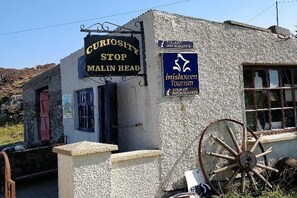 A small building with a sign reading "Curiosity Stop Malin Head" and another sign for "Inishowen Tourism." - Bree House Sleeps 16 With Free Parking (Malin)