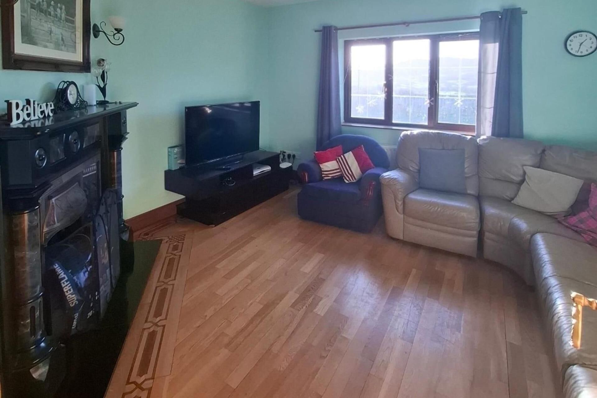 Una sala de estar con televisor, sofá, sillón y ventana con cortinas.