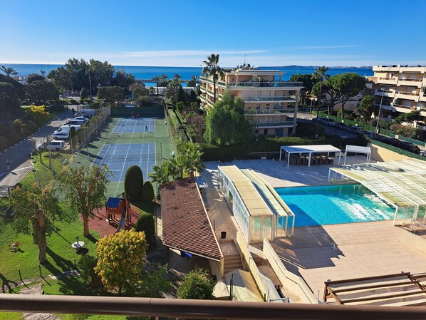 A residential area with a tennis court, swimming pool, and a view of the sea. - South-Facing Apartment (Saint-Laurent-du-Var)