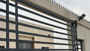 A gated entrance to a building with a modern design, featuring a metal gate and a security camera. - Perfect 7-bedroom house with stunning sunsets (Rosarito)