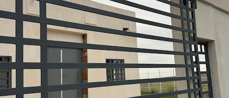 A gated entrance to a building with a modern design, featuring a metal gate and a security camera.