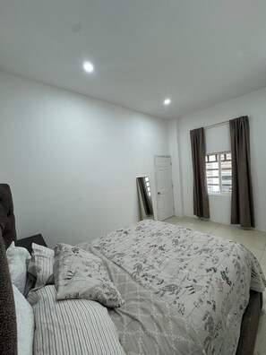 Een slaapkamer met een bed, een stoel, een deur en een raam met gordijnen.