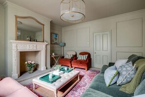 A living room with a fireplace, a mirror, a red armchair, a green sofa, and a patterned rug. - Luxury Central Townhouse / Sleeps 10 / Parking (Chester)
