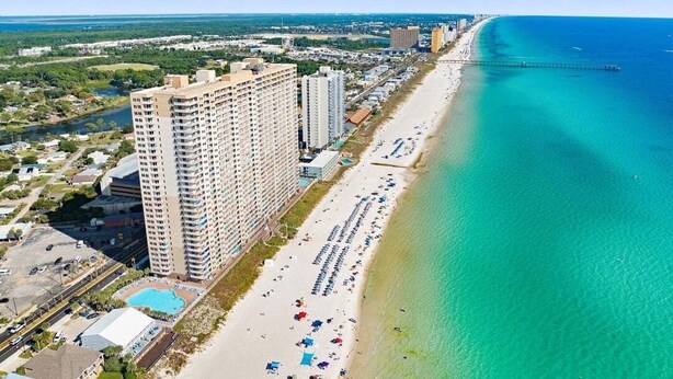 A high-rise hotel adjacent to a beach with clear turquoise waters and a pier extending into the ocean. - Emerald Escape 2007–Gulf Front–Sleeps 6 (Panama City Beach)