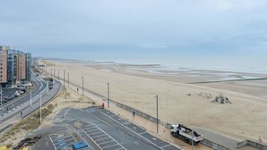 A coastal road with a beach in the background, a parking area, and a building with multiple floors. - Cosy apartment for 4 people with WIFI, TV, balcony and panoramic view (Bruges)