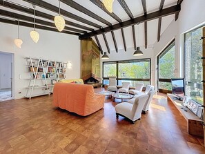 Ein großzügiger Wohnraum mit Kamin, großen Fenstern und einer Bücherwand.