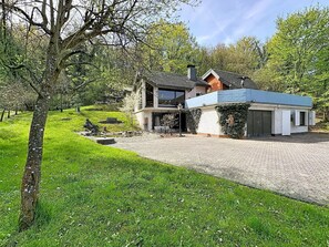 Ein modernes Haus mit befestigter Auffahrt, einer überdachten Terrasse und einem Garten mit Baum.