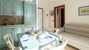 A dining area with a table set for four, a kitchen with teal cabinets, and a striped sofa. - Lovely apartment for 4 guests with WIFI, A/C and balcony (Taggia)
