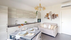 Eine moderne Küche mit weißen Schränken, einem Esstisch für vier Personen und einem Sofa im angrenzenden Wohnbereich.